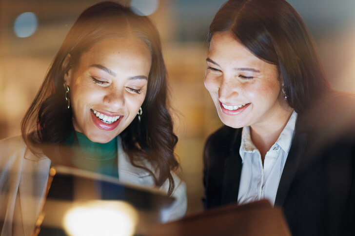 Two Ladies With Faces Lit Up By The Glow Of An Ipad